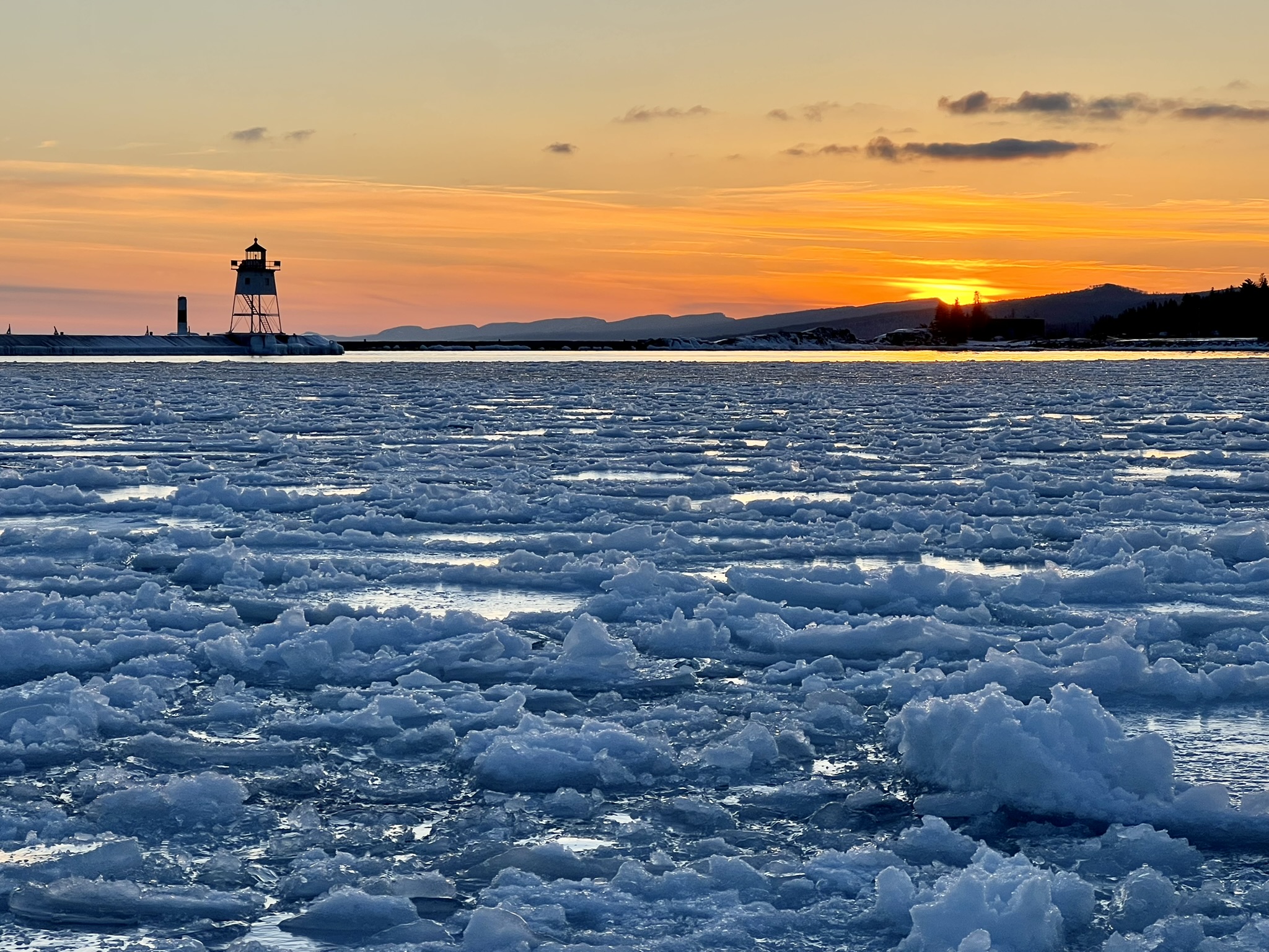Ice moving across the Grand Marais harbor at sunset.